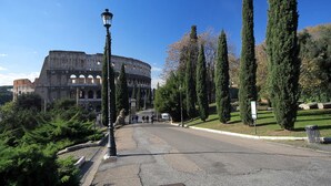 A view of the Colosseum with a street in the foreground, trees, and a lamppost. - Rome Colosseum Vacation Rental - Spacious Apartment Ancient Rome 3BR/2B Wi-Fi (Roma)