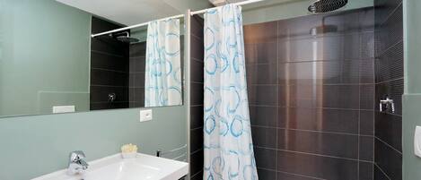 Een moderne badkamer met een wit wastafel, een spiegel, een douche met gordijn en donkere betegelde wanden.