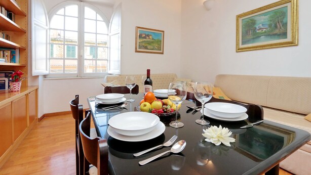 A dining area with a table set for two, a window, and a painting on the wall. - Rome Colosseum Vacation Rental - Spacious Apartment Ancient Rome 3BR/2B Wi-Fi (Roma)