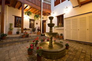 Un patio con una fuente de piedra, plantas en macetas y una escalera de madera que lleva a un nivel superior.