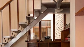 A wooden chair with a woven seat in a room with a staircase, bookshelves, and a sofa.