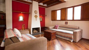A living room with a fireplace, wooden beams, a sofa, and a striped cushion.