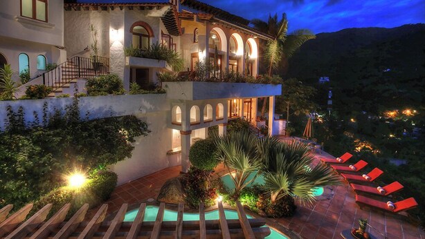 Una villa lujosa con piscina, zona de estar al aire libre y montañas al fondo.