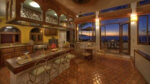 Una cocina amplia con una isla grande, armarios de madera y vistas al atardecer a través de puertas de cristal.