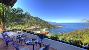 Terraza con mesa y sillas, con vista al mar, barcos y una playa.