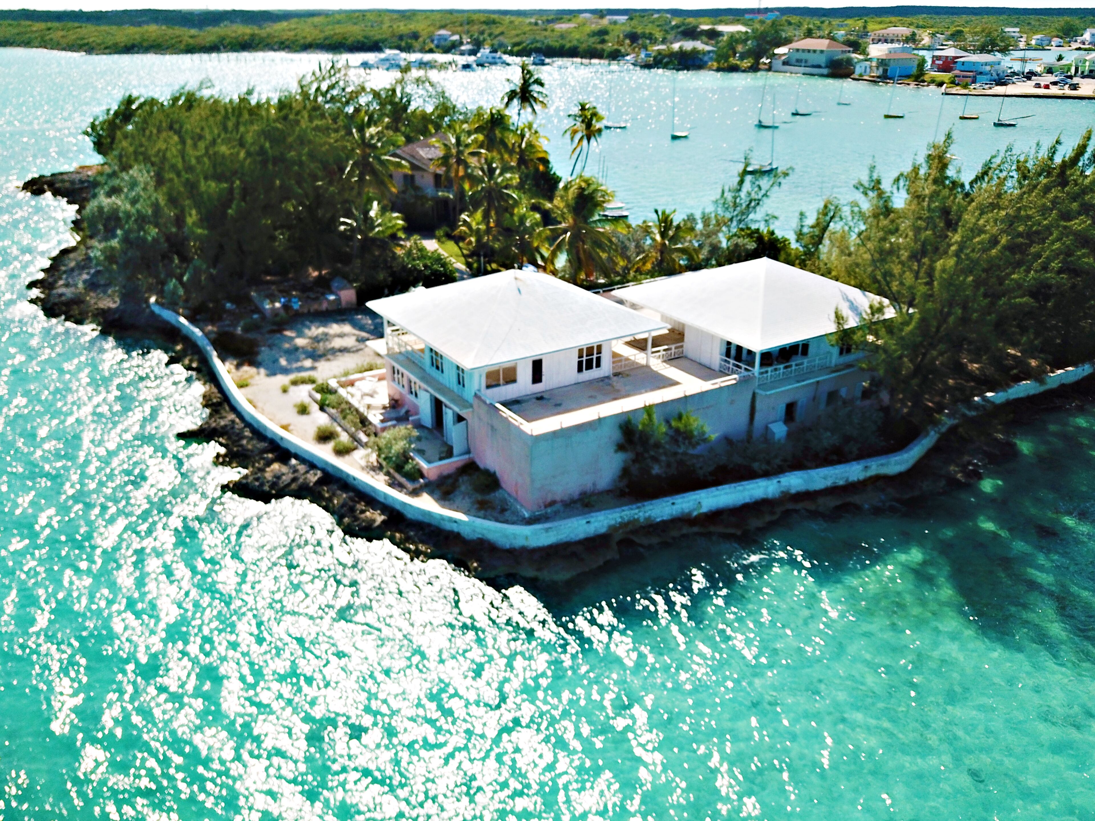 A coastal house with a white exterior, surrounded by a rocky shoreline and clear turquoise waters.