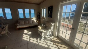 A spacious living room with a sofa, a chair, and a bookshelf, large windows with a view of the sea, and a ceiling fan. - Centrally located - Gorgeous view of Elizabeth Harbour  (George Town)