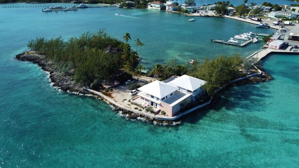 An aerial view of a small island with a single large building surrounded by clear turquoise waters and lush greenery. - Centrally located - Gorgeous view of Elizabeth Harbour  (George Town)