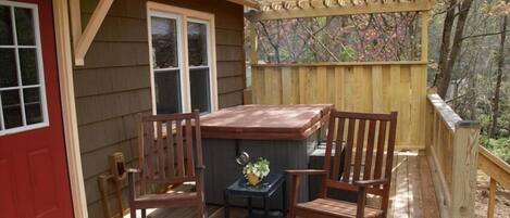 A wooden deck with a hot tub, two rocking chairs, and a small table with a plant.