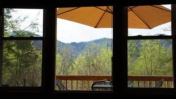 Blick aus einem Fenster mit Holzwertkasten und Tisch auf eine bewaldete Berglandschaft.