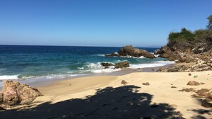 Ein Strand mit klarem Himmel, Felsformationen und ruhigen Wellen.