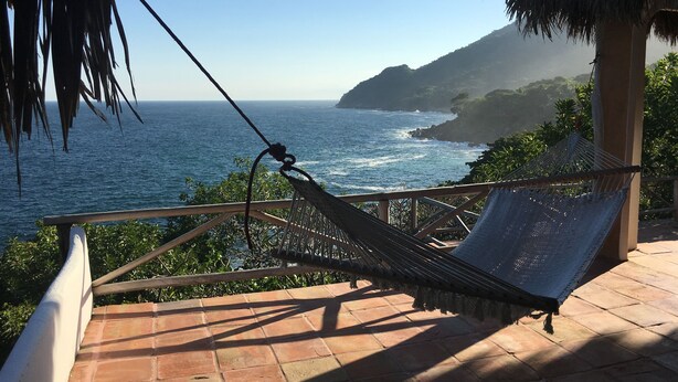 Eine Hängematte auf einer Terrasse mit Blick auf den Ozean, im Hintergrund ein Berg.