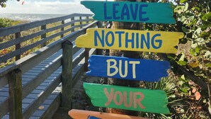 Une pancarte en bois avec des lettres colorées, fixée sur le tronc d’un arbre, à côté d’une passerelle en bois.