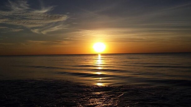 Un coucher de soleil sur une mer calme, avec un horizon dégagé.