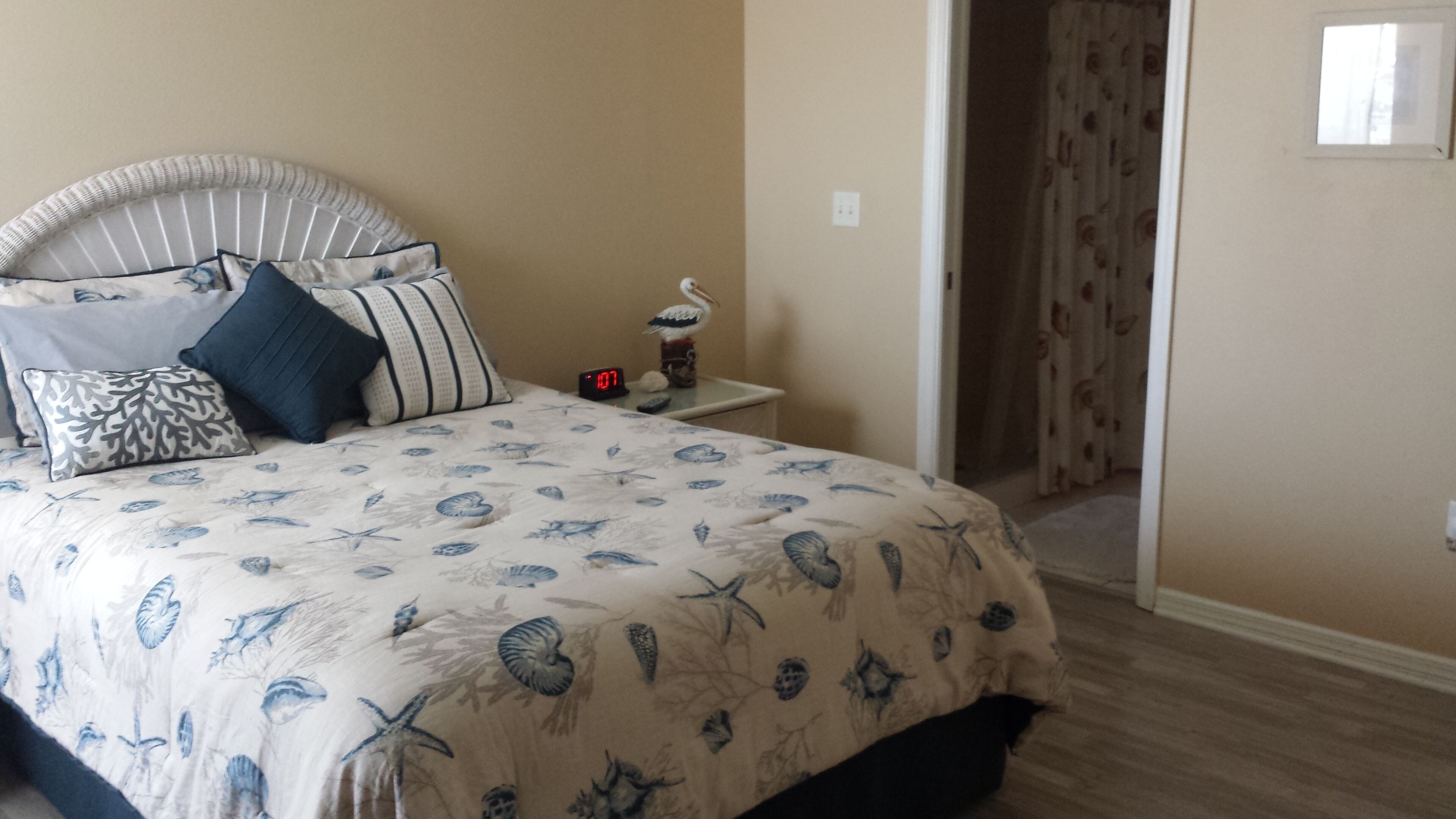 A bedroom with a bed, pillows, a nightstand, a digital clock, and a door leading to another room.