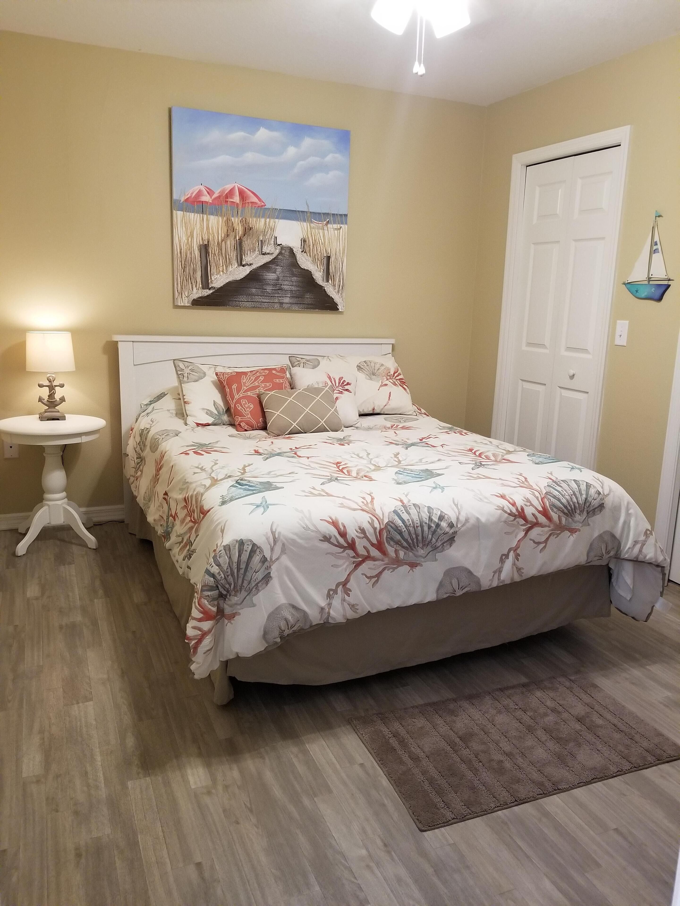 A bedroom with a bed, a nightstand, a lamp, a painting, and a door.