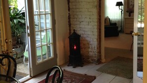 A room with a brick wall, a door leading outside, a green chair, a table with plates, and a patterned rug.
