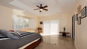 A bedroom with a bed, a ceiling fan, a chair, a small table, and a window with blinds. - Family Friendly Home, with a Man Cave! (Keaau)