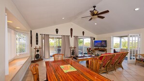 A spacious living room with a wooden dining table, comfortable seating, a ceiling fan, and a television. - Family Friendly Home, with a Man Cave! (Keaau)