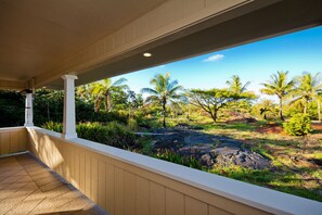 A covered outdoor area with a view of a tropical landscape including palm trees and a rocky terrain. - Family Friendly Home, with a Man Cave! (Keaau)