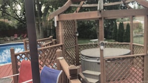 A view through a window with a metal grill, featuring a patio area with outdoor furniture and a red-roofed structure.