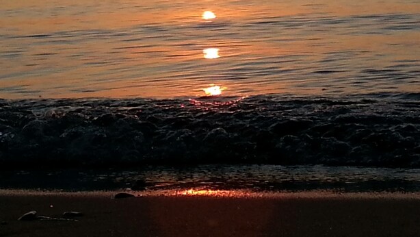 A sunset over a calm sea with gentle waves at the shore.