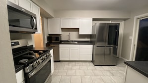 A modern kitchen with white cabinets, stainless steel appliances, and a tiled floor.