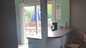 A kitchen area with a counter, two wooden chairs, a trash bin, and a view of an outdoor deck with umbrellas.