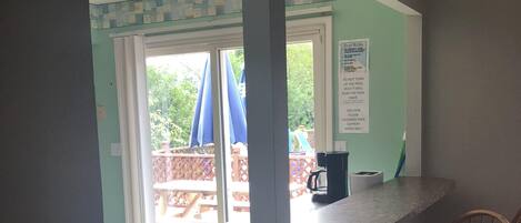 A kitchen area with a counter, two wooden chairs, a trash bin, and a view of an outdoor deck with umbrellas.