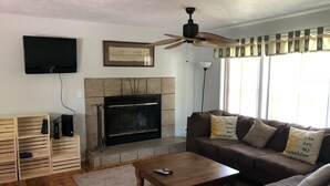 A living room with a fireplace, a ceiling fan, a television mounted on the wall, and a sofa with decorative pillows.