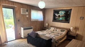 Une chambre à coucher comprenant un lit, une petite table de chevet, une commode, une fenêtre avec des rideaux, un climatiseur fixé au mur et une tapisserie.