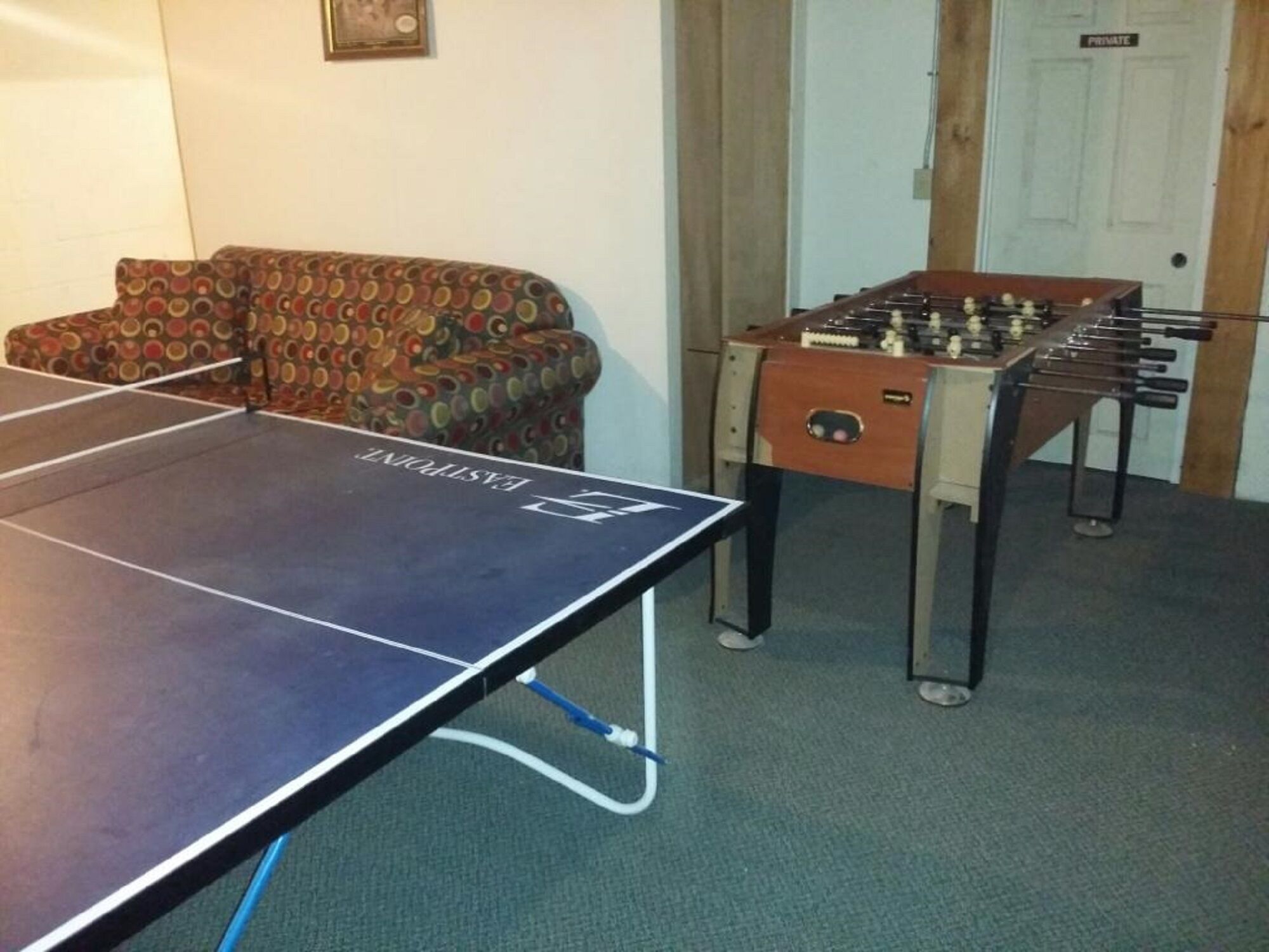 A room with a foosball table, a ping pong table, and a patterned sofa.