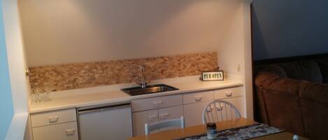 A compact kitchen with a sink, a dishwasher, and a countertop. There is a sign that reads "PUB OPEN" on the countertop.