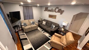 Ein Wohnzimmer mit einer Couch, zwei Sesseln, einem Couchtisch, einem Fernseher und einem Schild mit der Aufschrift 'Music City'.