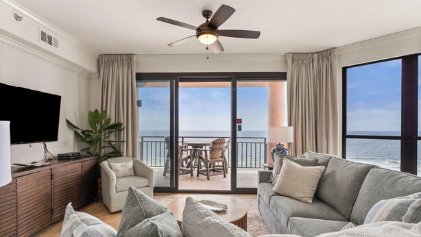 A modern living room with a flat-screen TV, a ceiling fan, and a large window with a view of the ocean. - Top Rental at SEACHASE!!! Totally remodeled!!! (Orange Beach)