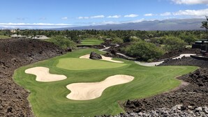 En golfbane med bunkers, putting green og udsigt til fjerne bjerge.