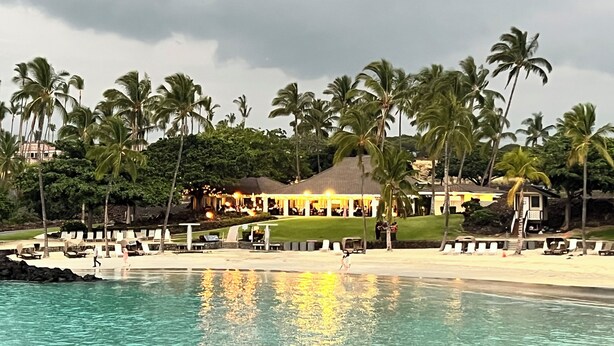 Et resort med pool, palmer og en bygning med stråtækt tag.