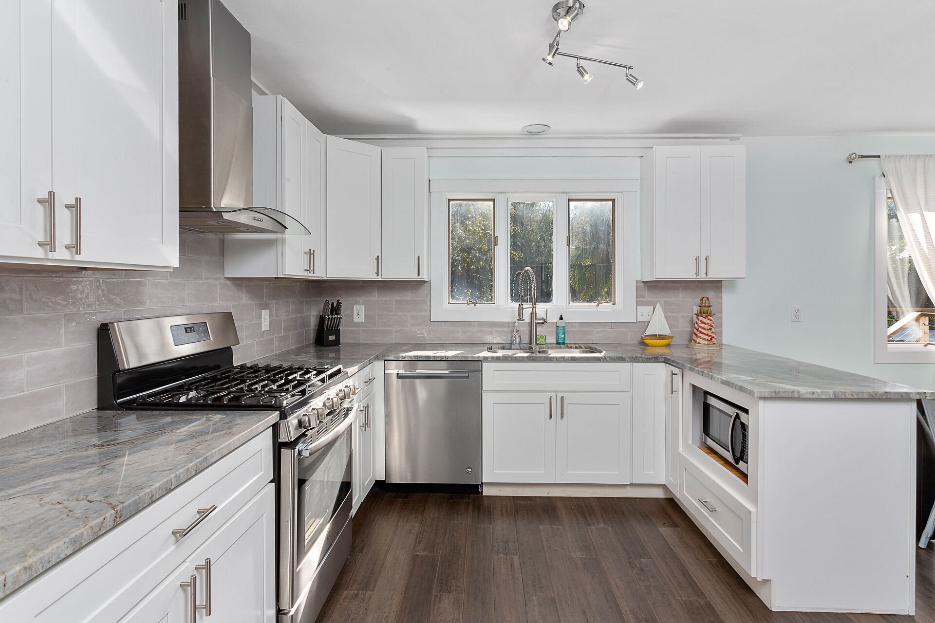 Una cocina moderna con armarios blancos, electrodomésticos de acero inoxidable y un ventanal que proporciona luz natural.