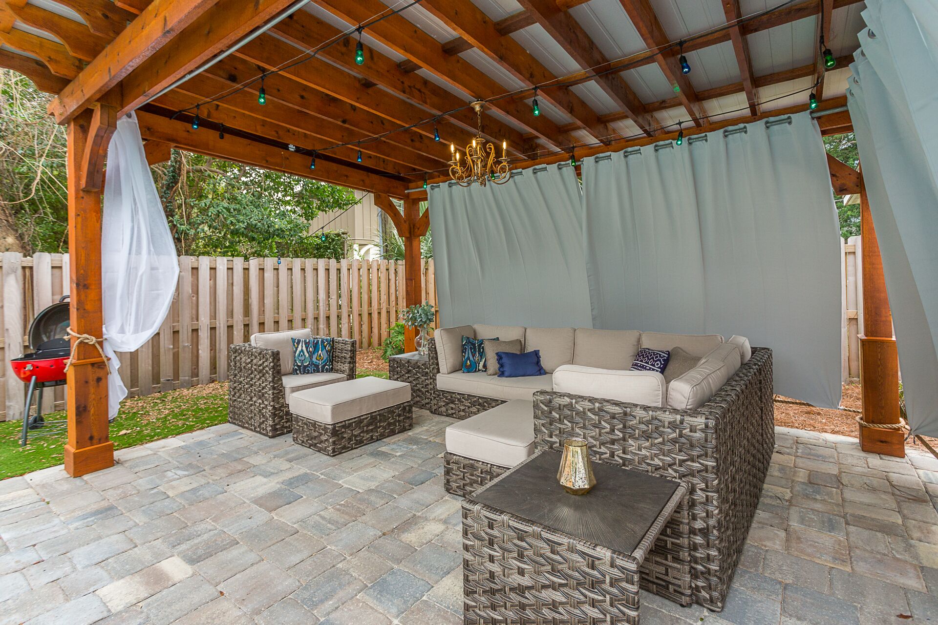 An outdoor patio with a covered seating area, stone flooring, and a pergola with string lights.