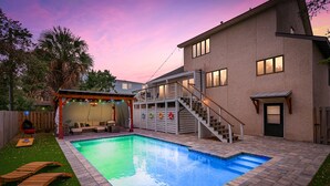 Ein Garten mit Pool, einer überdachten Terrasse und einem zweigeschossigen Haus.