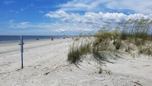 Ein sandiger Strand mit blauem Himmel und vereinzelten Wolken.