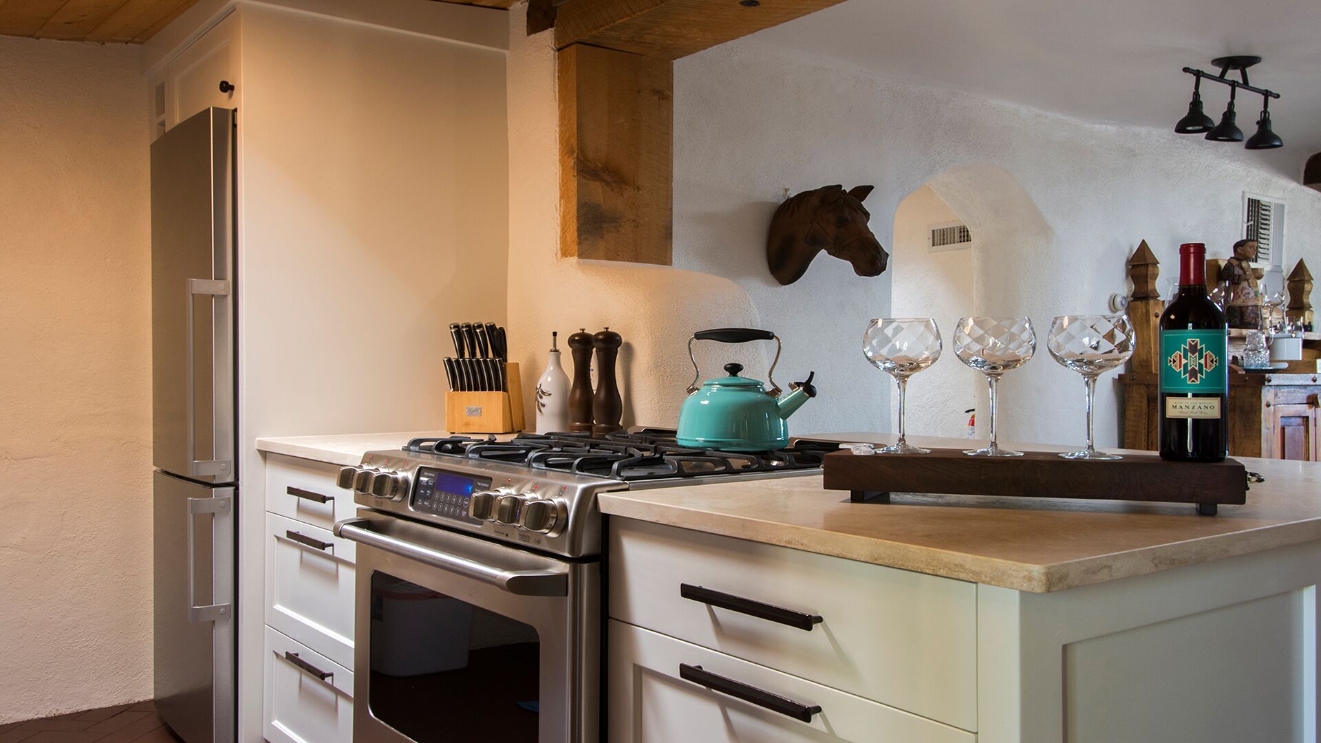 A kitchen with a stove, oven, and refrigerator. There are wine glasses and a bottle on the counter.