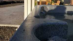 Una bañera de piedra con asiento integrado, una silla de madera y vista a un jardín con arbustos de lavanda.