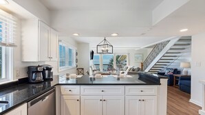 A modern kitchen with white cabinetry, a black countertop, and a central island. There is a staircase leading to a balcony with a view.