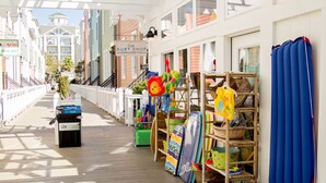 A wooden promenade with shops, including a surf shop and a cream shop, along a white fence.