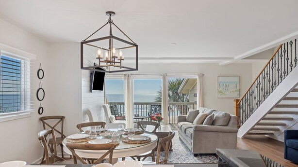 A spacious living area with a dining table set for four, a comfortable sofa, and a staircase leading to an upper level.
