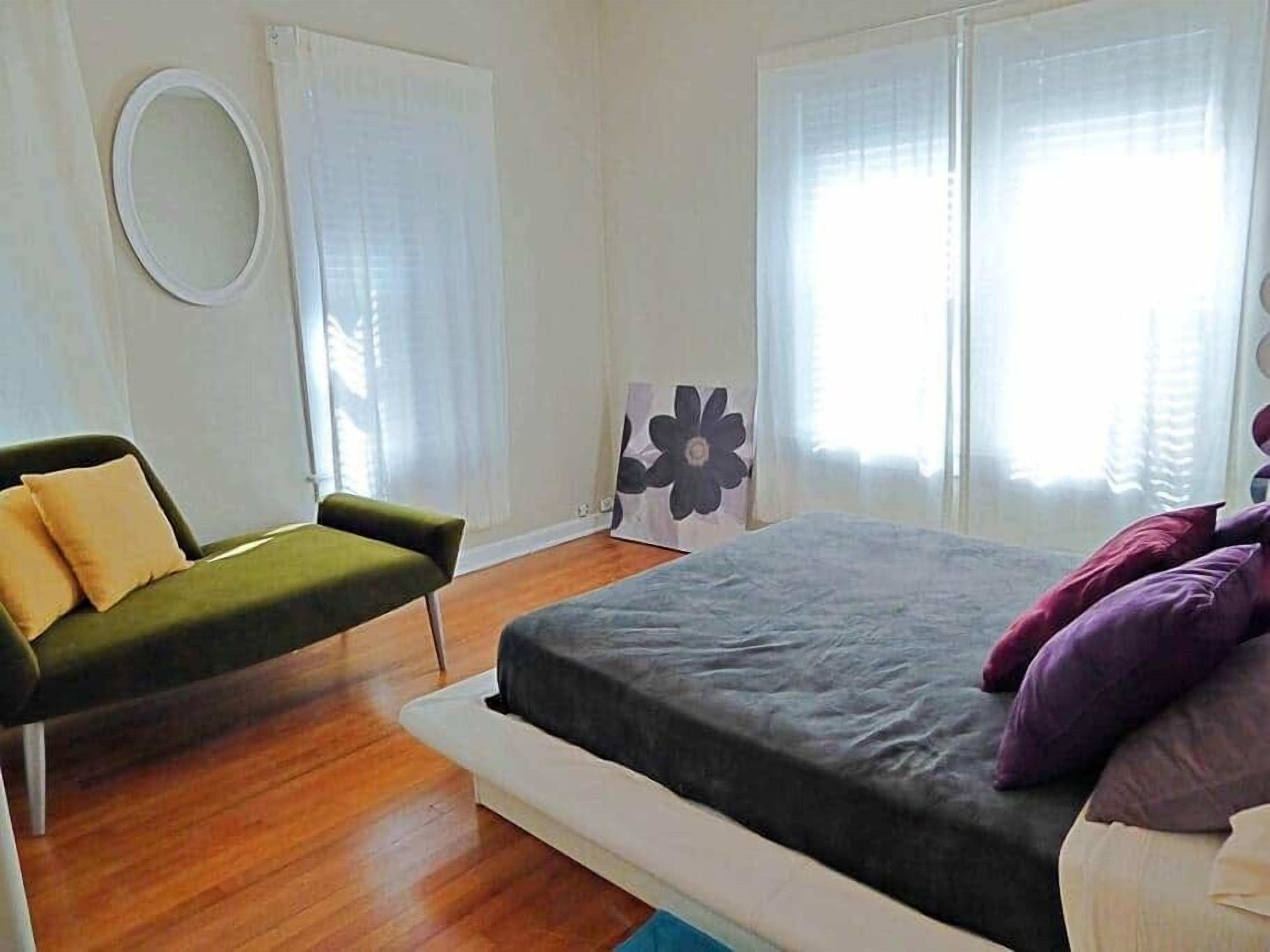 A bedroom with a bed, a green sofa, and a wall-mounted circular mirror.