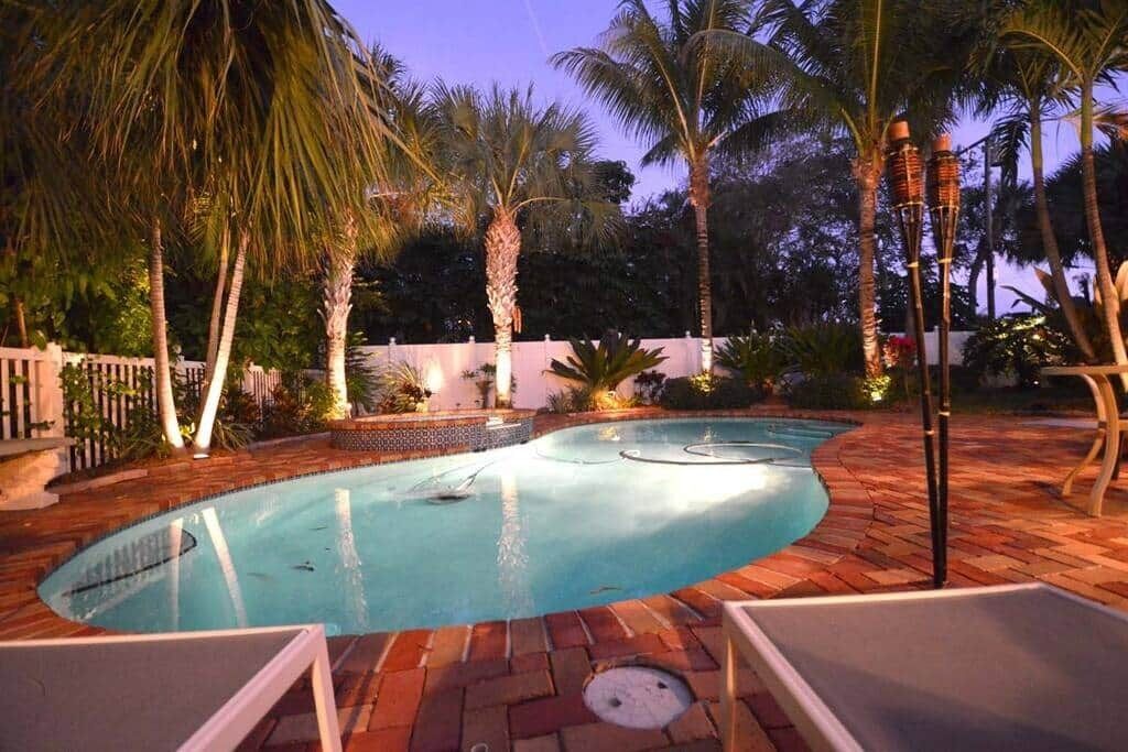 Ein Pool mit geschwungener Kante, umgeben von Palmen und einer Pflasterterrasse.
