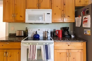 Una cocina con gabinetes de madera, un microondas blanco, una estufa y varios electrodomésticos.