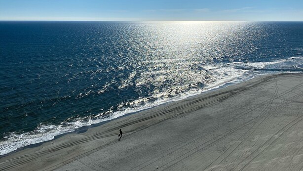 Een strand met een heldere lucht en de zon die op het water schijnt.